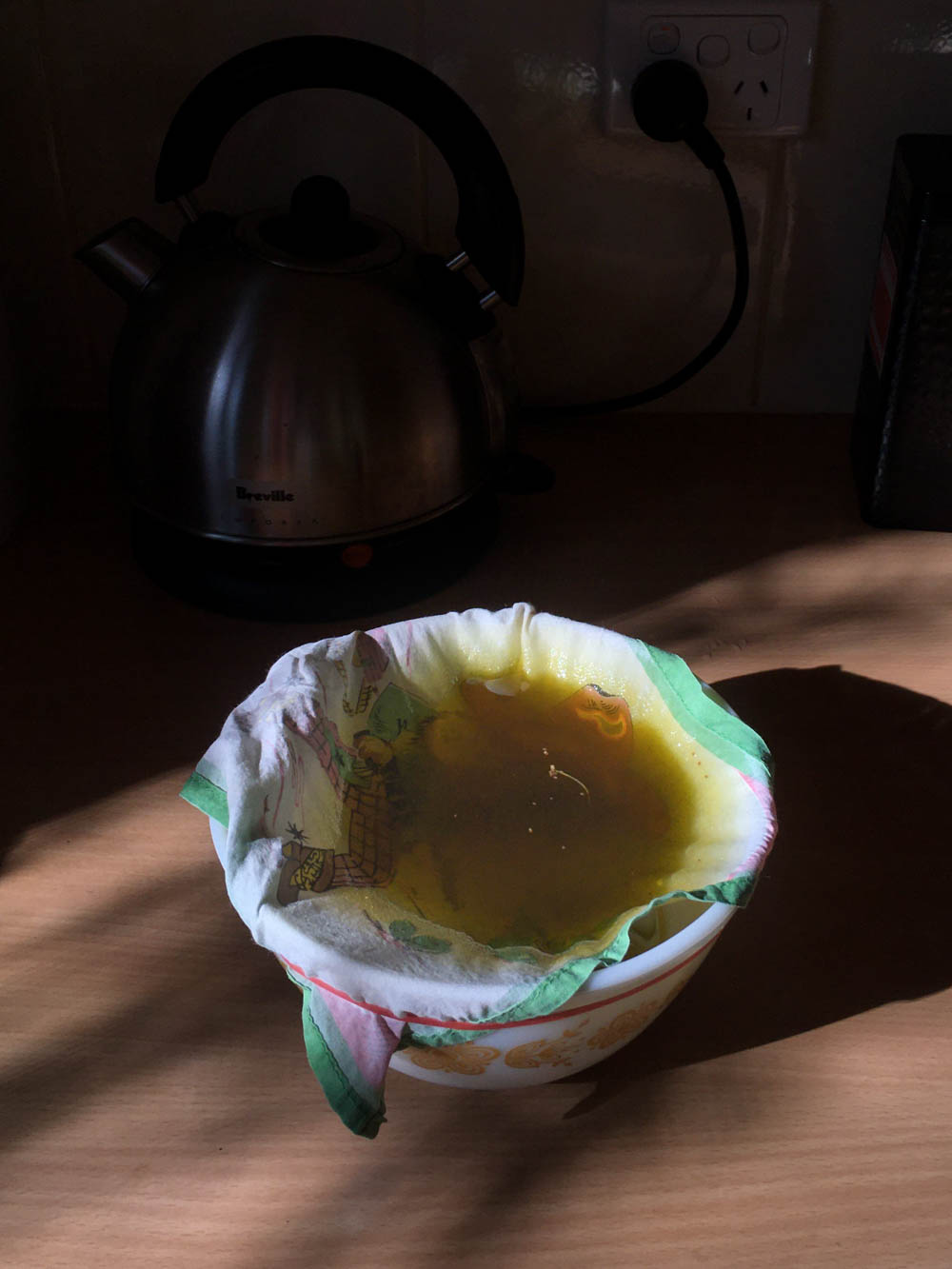 A handkerchief stretched over a bowl, which is straining the olive oil from the calendula petals.