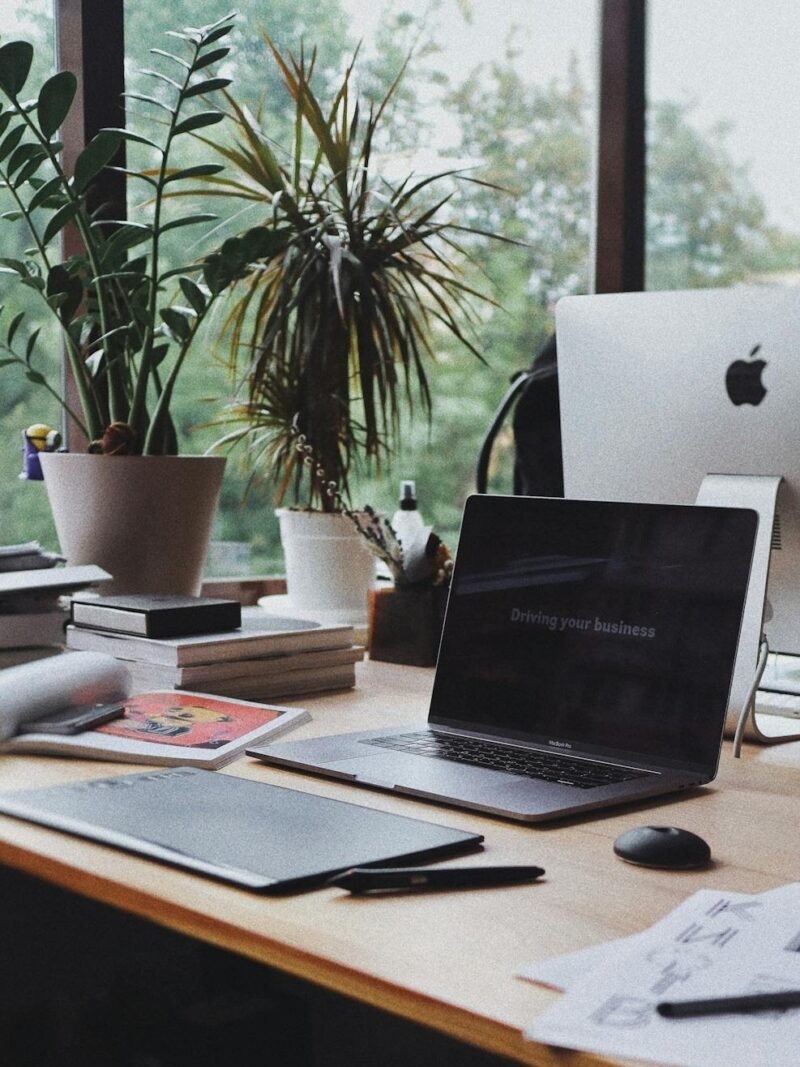 A computer sitting atop a wooden desk, surrounded by plants.