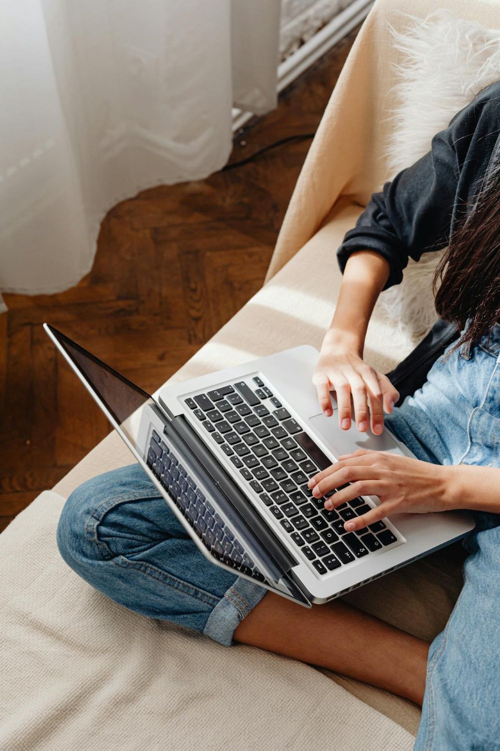A woman sitting on a sunlight couch, reviewing her high-converting sales page on a laptop computer.